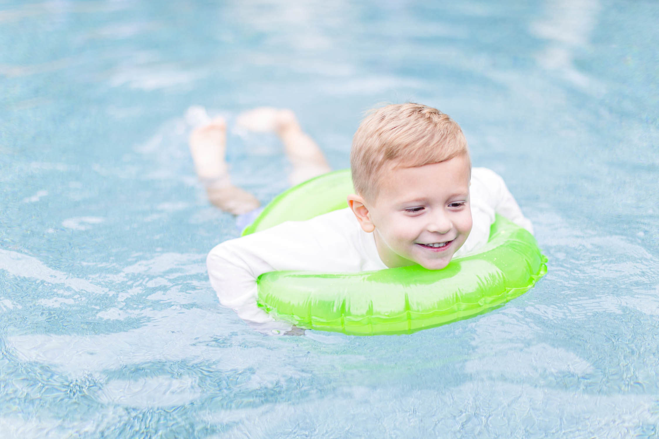 Boy smiles and swims with a green tube float during pool party mini sessions by Elle Bea Photography in July 2022 in Rossville, Georgia