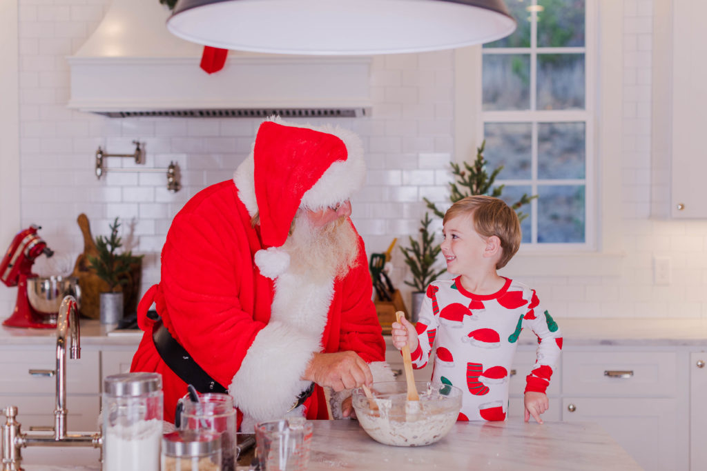 Little boy smiles at and bakes cookies with Santa during Baking with Santa mini sessions