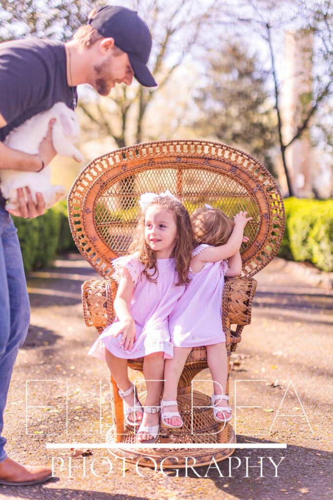 Toddler girl squirms away from white bunny while sister awaits holding him at live bunny mini sessions in Chickamauga, Georgia