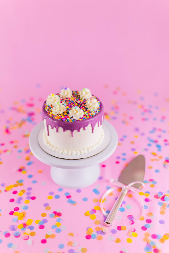 Lavender confetti ice cream cake on pink tablecloth with confetti and silver cake server