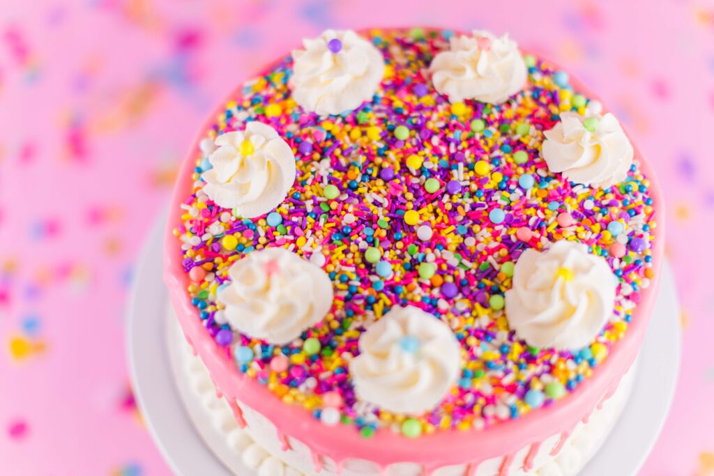 Pink confetti ice cream cake by Ice Dream Cakes Chattanooga sits on a pink table with multi colored confetti