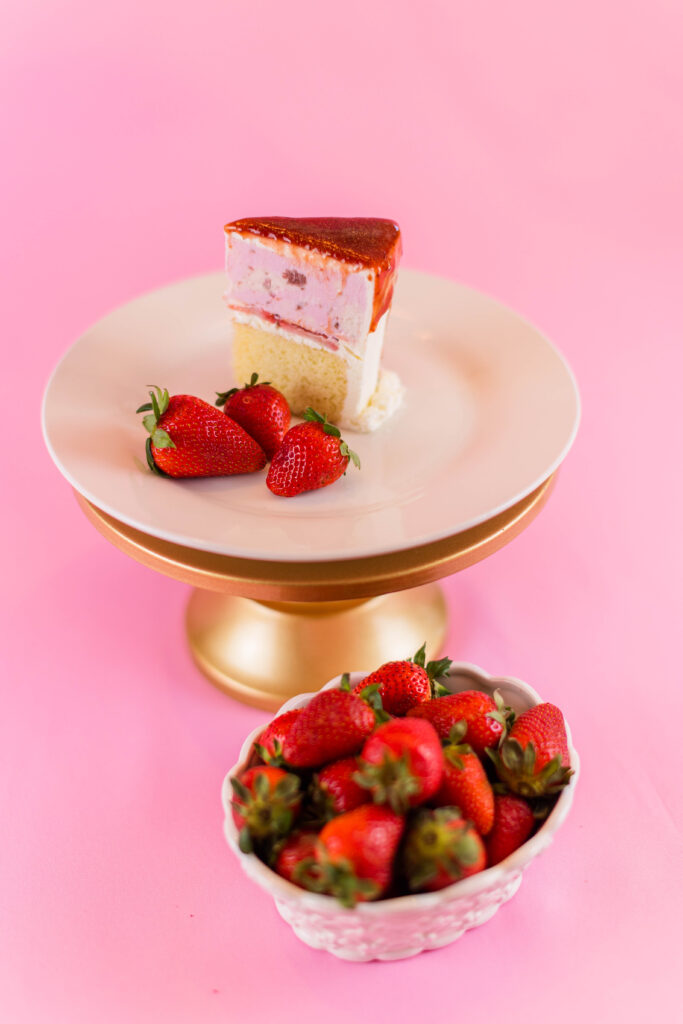 Slice of strawberry ice cream cake with bowl of strawberries