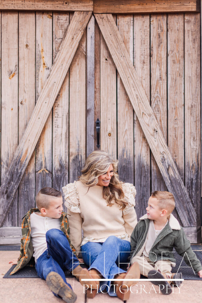 Grandmother smiles with grandsons in front of rustic wood barn door at Mountain Cove Farms