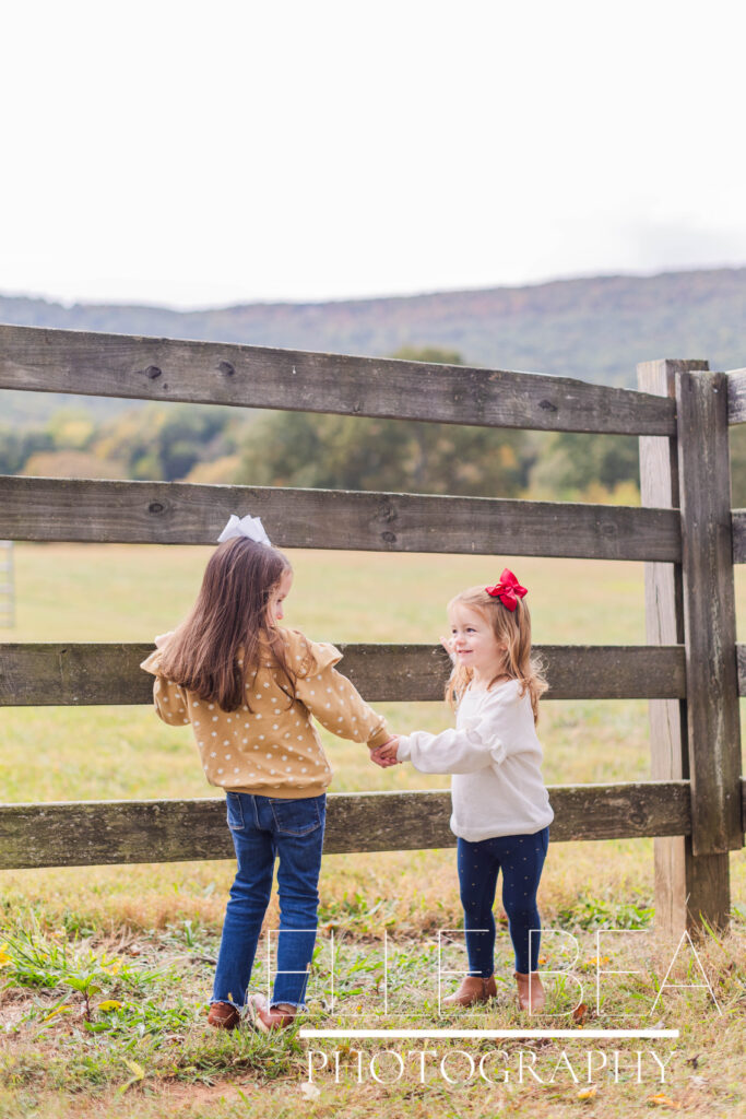 Sisters smile together at a rustic fence at Mountain Cove Farms in Chickamauga, Georgia