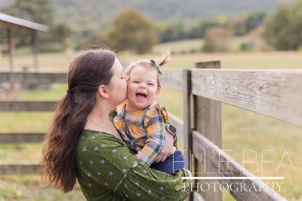 Mom kisses baby girl at Mountain Cove Farms during cloudy fall mini sessions