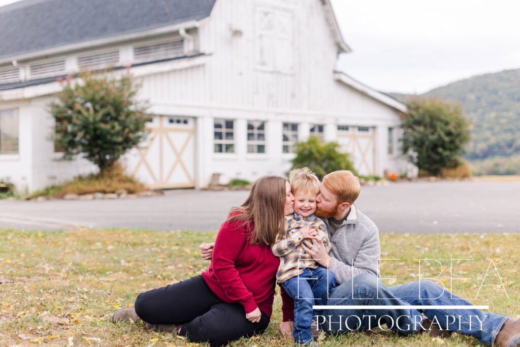 Mom and dad kiss little boy in front of the show barn at Mountain Cove Farms