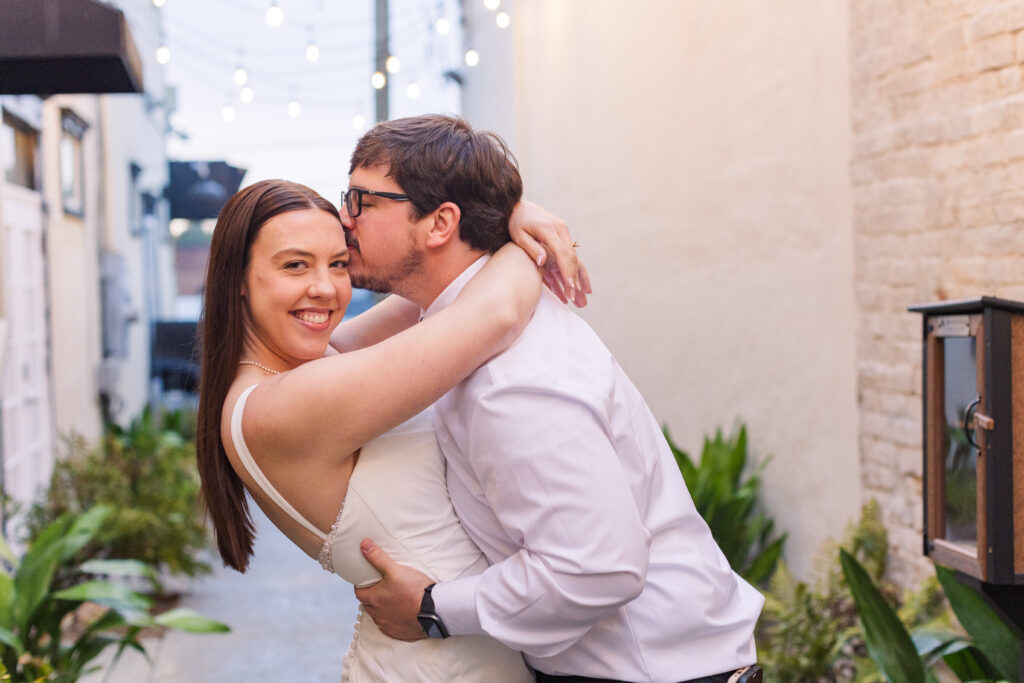 Husband kisses his brand new wife in an alleyway with bistro lights outside their wedding reception, captured by their Chickamauga wedding photographer